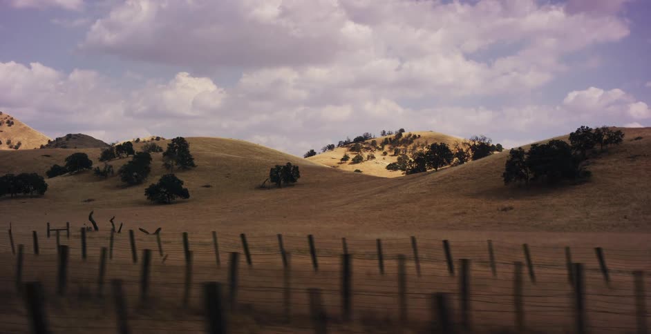 A slow tracking shot reveals golden rolling hills and oak trees in the rural countryside under a cloudy sky