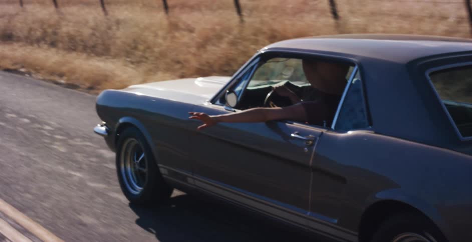 Slow motion tracking shot of a carefree woman driving a classic muscle car with her arm out the window on a sunny country road