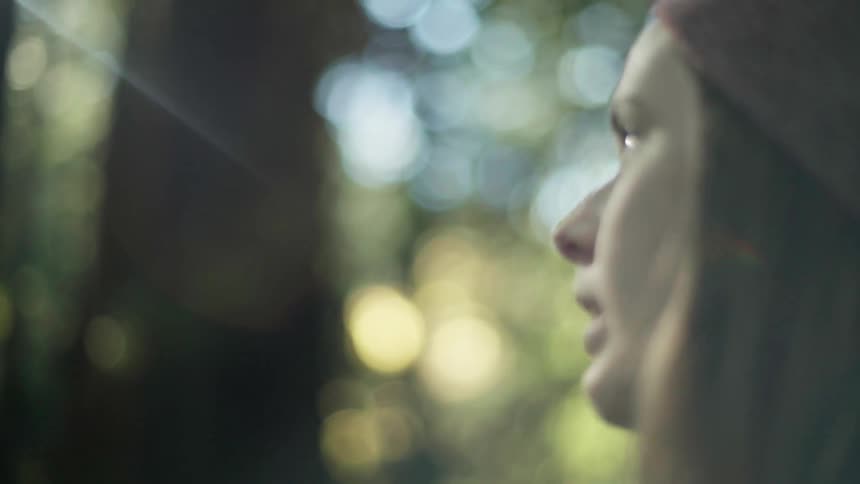A woman wearing a green sweater and purple beanie takes pictures in the forest