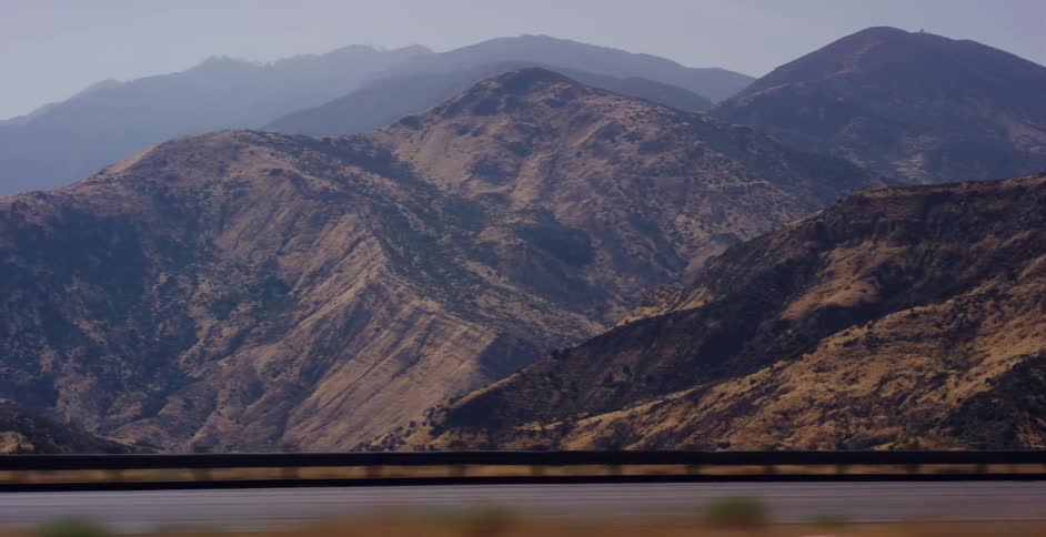 A scenic view of a vast, arid mountain range as seen from a moving vehicle on a highway