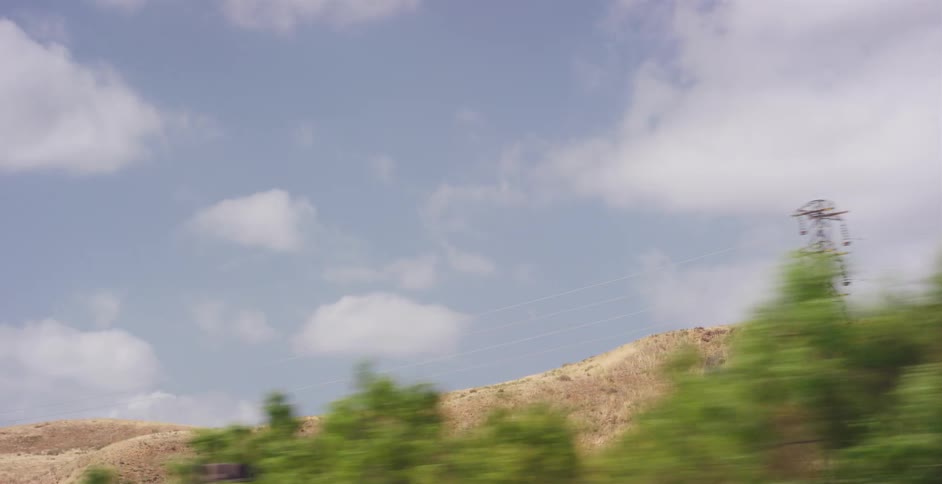 A scenic drive past golden hills and power lines under a cloudy blue sky