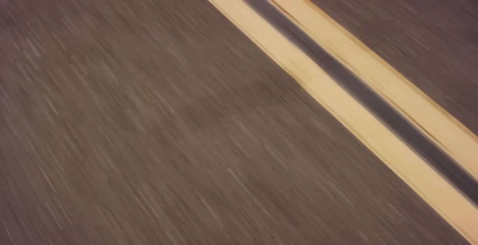 A fast-paced view of a road gives way to a classic silver Ford Mustang parked on a country road amidst golden hills