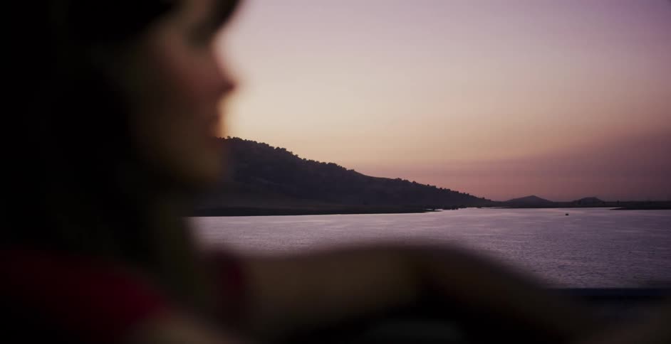 A contemplative woman drives along a serene lake, with the focus shifting from her to the beautiful dusk scenery