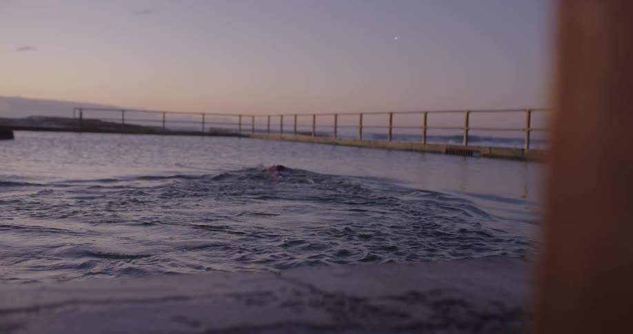 A female swimmer dives into a tranquil ocean rock pool at dawn and begins to swim freestyle in slow motion