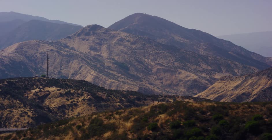 A slow, sweeping view reveals a vast and hazy mountain range in a dry, arid landscape