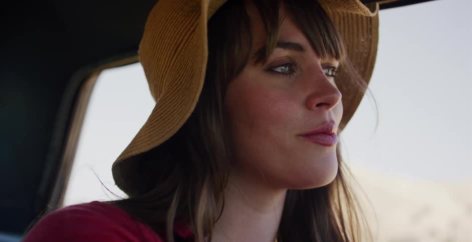 A thoughtful woman in a sun hat gazes out the window while riding in a car on a sunny day