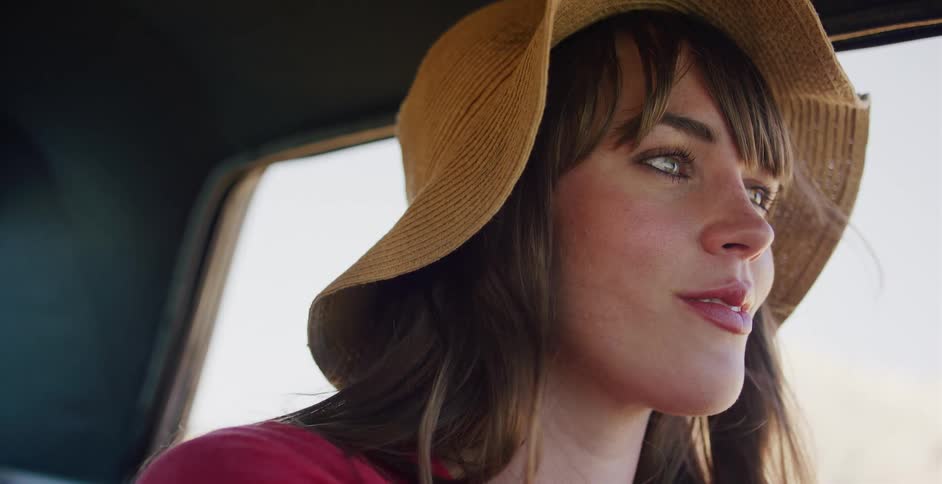 A contemplative woman in a sun hat gazes out the window while riding in a car on a sunny day