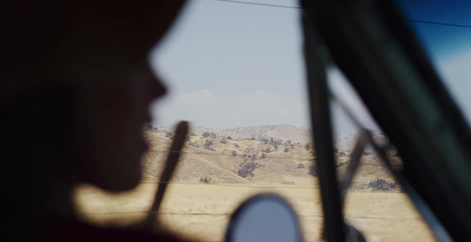 A slow motion view from inside a moving vehicle reveals the vast, golden hills of a dry, rural landscape passing by