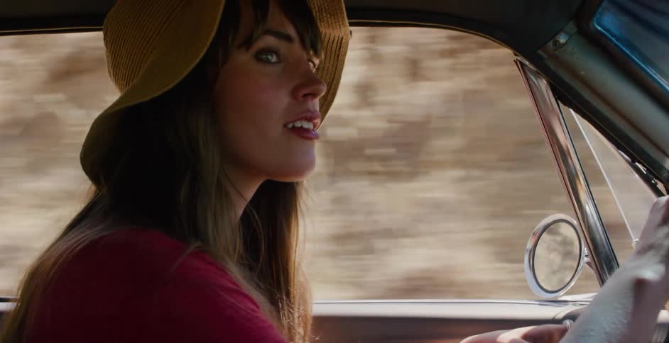 Side profile of a woman wearing a stylish hat as she drives a vintage car down a scenic road on a sunny day