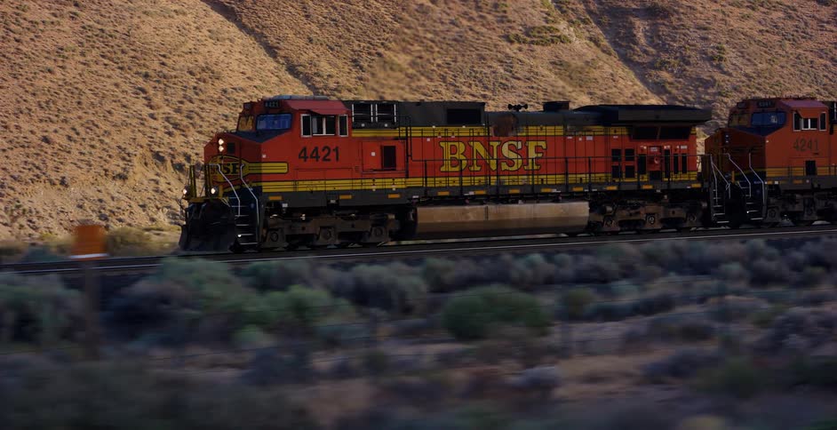 A BNSF freight train travels through a vast desert landscape at golden hour