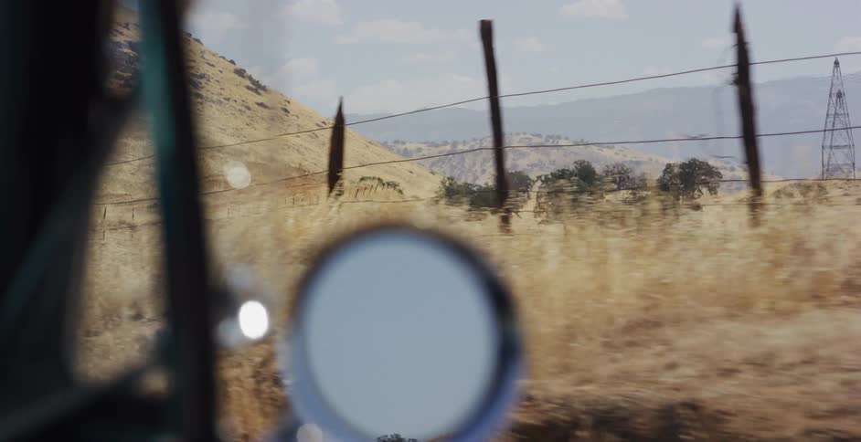 A slow-motion drive through the arid countryside, with a focus on the landscape reflected in the car's side-view mirror