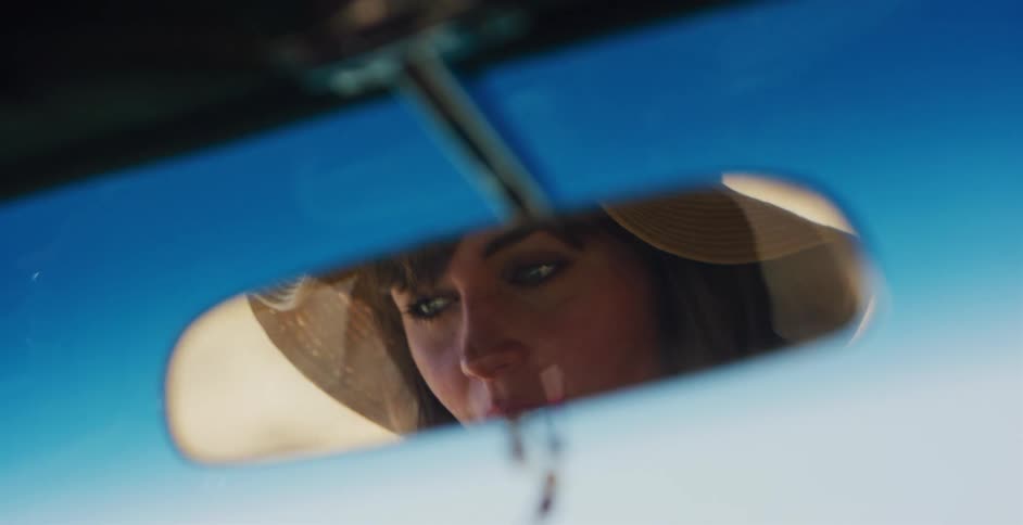 A woman's pensive eyes are seen in the reflection of a car's rearview mirror on a sunny summer day
