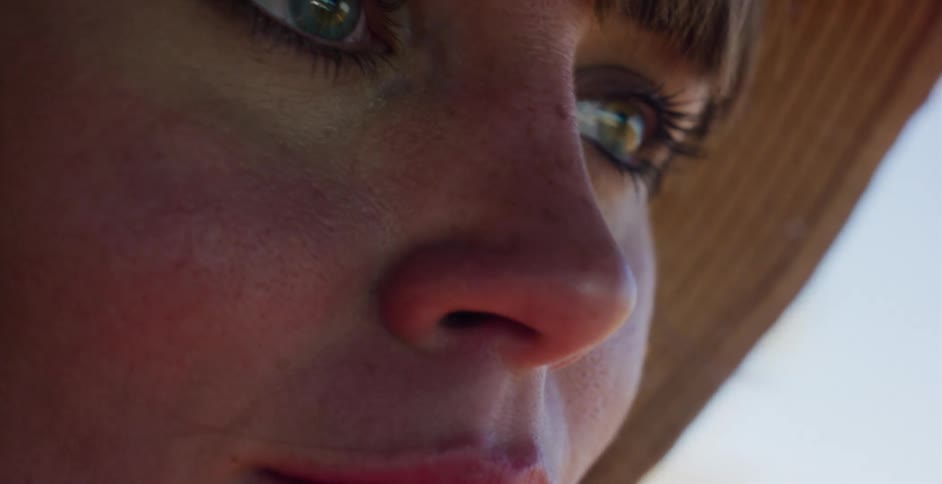 An intimate close-up of a woman's serene face with green eyes, wearing a straw hat in the warm sunlight