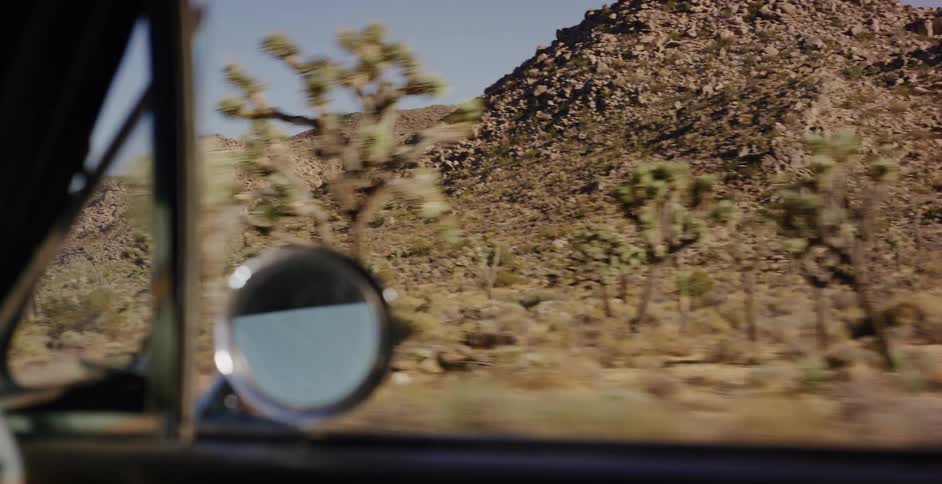 A scenic drive through a sun-drenched desert landscape, with Joshua trees and rocky mountains blurring past the car window