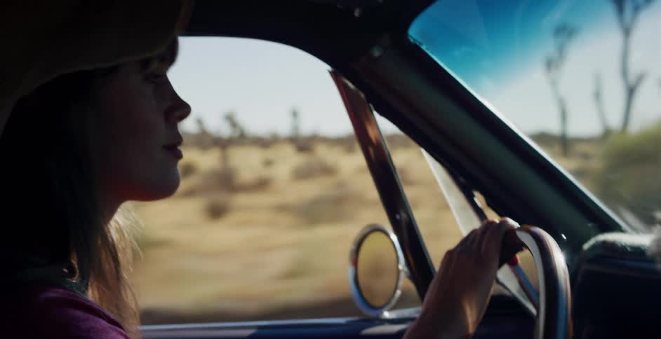 A woman in a hat drives a vintage car on a road trip through the sunny desert