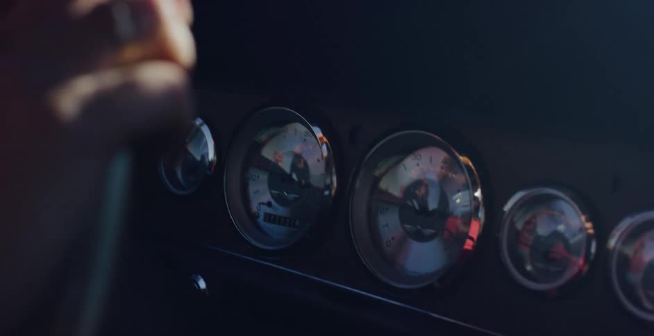 Sunlight reflects off the classic chrome gauges of a vintage car's dashboard as it's being driven