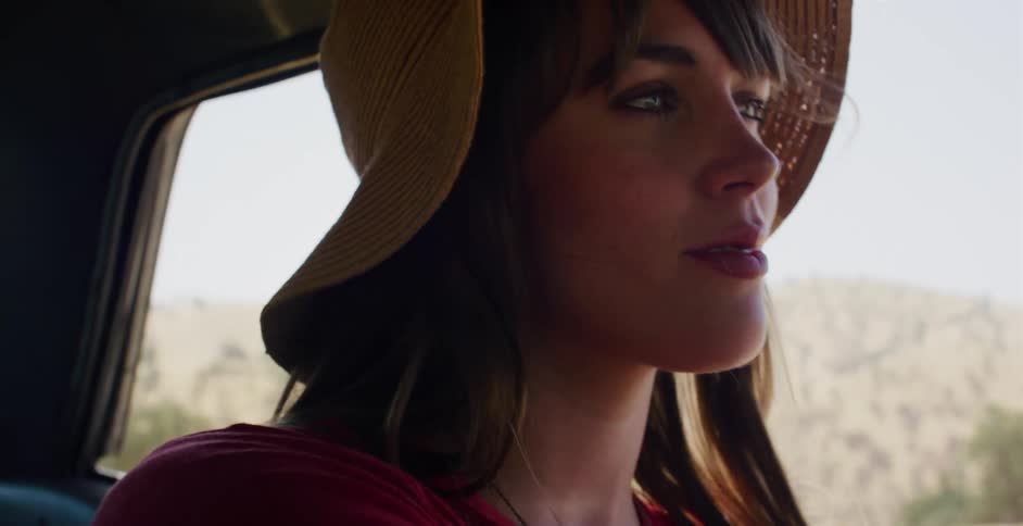 A pensive young woman in a straw hat enjoys a sunny road trip, looking out the passenger window as the landscape rushes by
