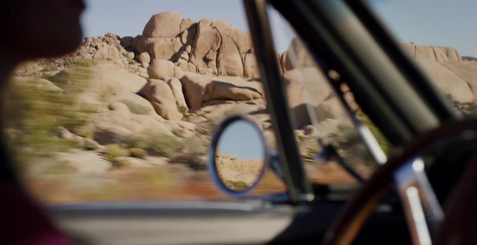 A passenger's view from a vintage car speeding through a sunny desert landscape of unique rock formations