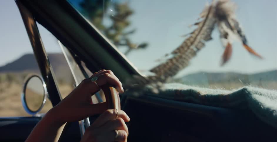 A woman's hands grip the steering wheel of a classic convertible during a bohemian-style road trip through the sunny desert