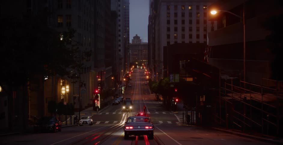 Static long shot of a vintage car parked on a steep, dimly lit downtown street at dusk in San Francisco