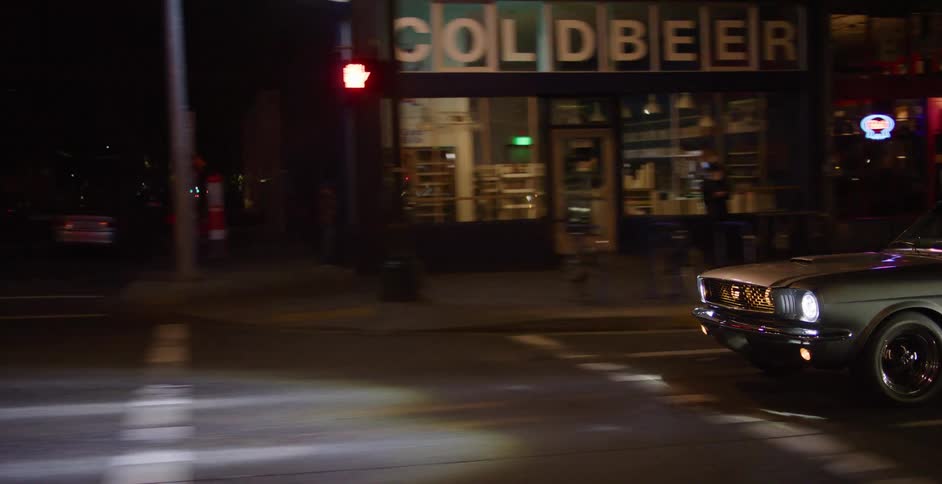 Tracking shot of a vintage muscle car driving down an urban street illuminated by city lights at night