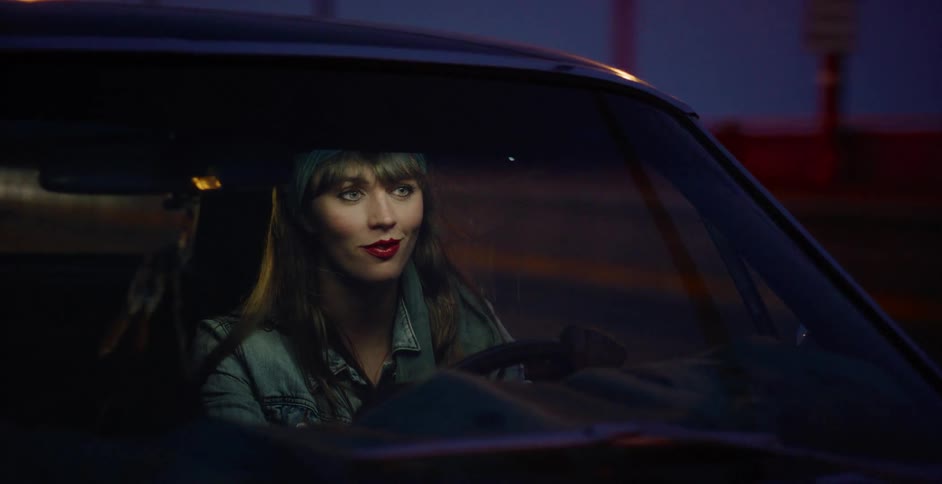A stylish woman with red lipstick drives her classic car through the city at night