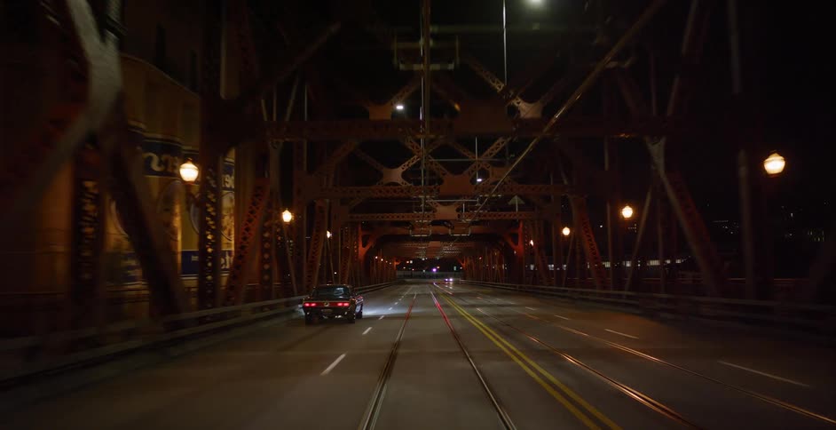 Cinematic POV shot following a car as it drives across a large industrial bridge at night