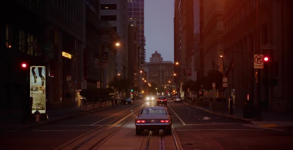 A vintage muscle car cruises down a quiet downtown San Francisco street on cable car tracks at twilight