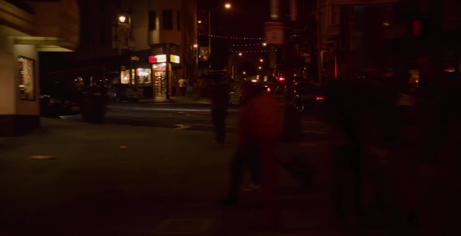 Dark silhouettes of pedestrians cross a busy city street at night as cars drive by