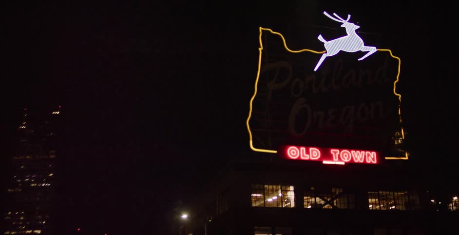 Driving through downtown Portland at night as the camera tilts up to the historic 'Portland, Oregon, Old Town' neon sign