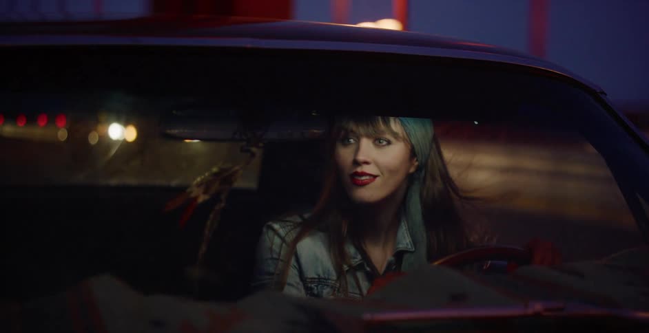 A stylish young woman with red lipstick drives her classic car across the Golden Gate Bridge at night