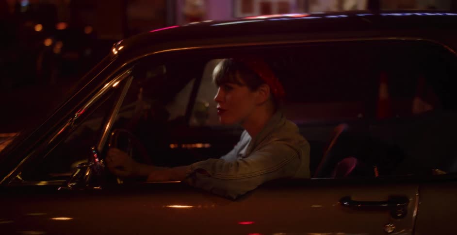 A retro-styled woman drives a vintage car through city streets illuminated by neon lights