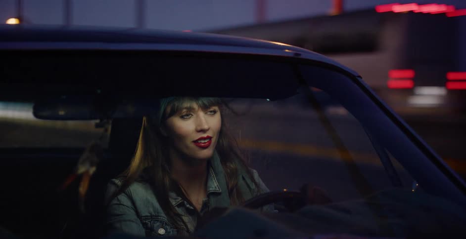 A stylish young woman with red lipstick and a bandana enjoys a nighttime drive in her classic car