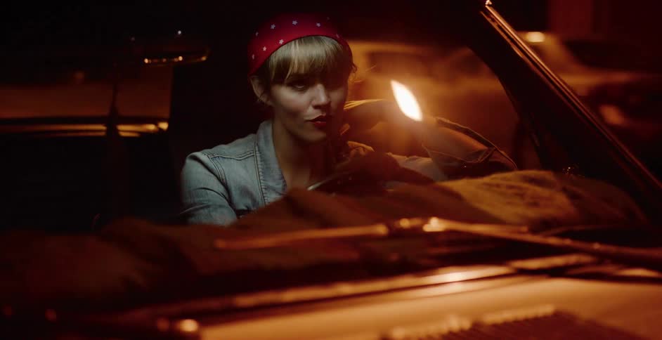 A beautiful woman with a retro look sits in a classic convertible car and waits for someone on a city street at night