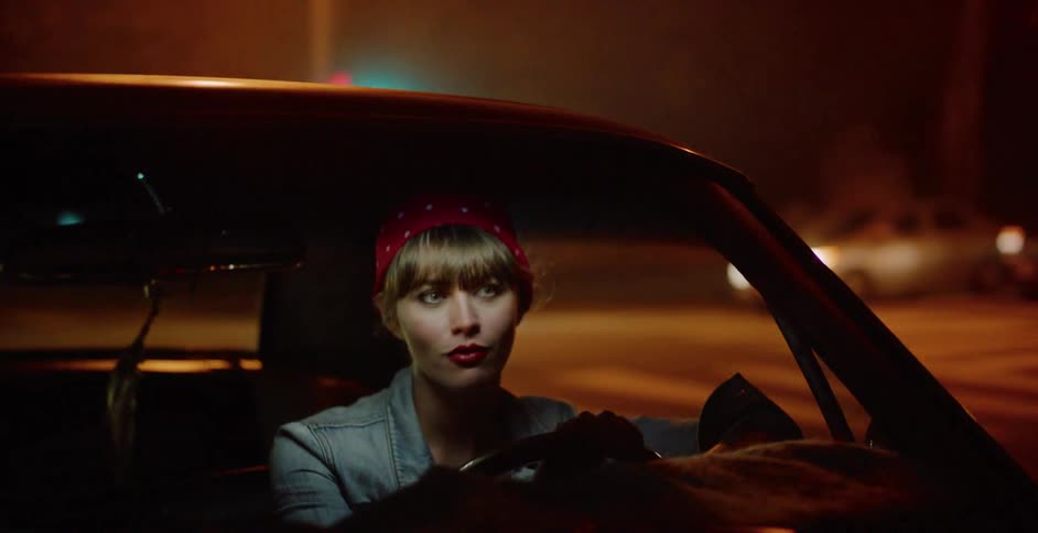 A stylish woman with a red bandana drives her vintage car through the city streets at night