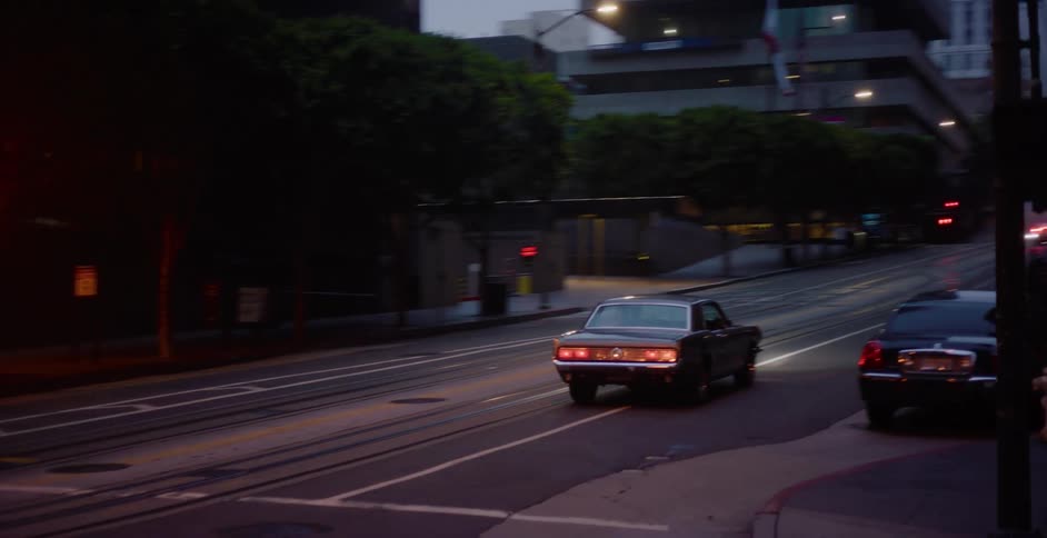 A classic muscle car turns onto a steep, foggy San Francisco street with cable car tracks at twilight