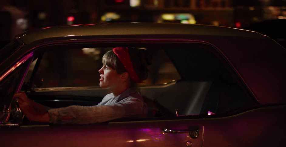 A cool young woman with a vintage style drives her classic American car through the city streets at night