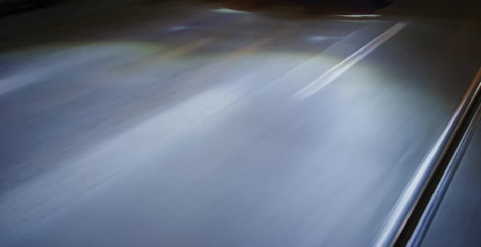 A woman cruises in slow motion in a classic muscle car across an empty city bridge at night