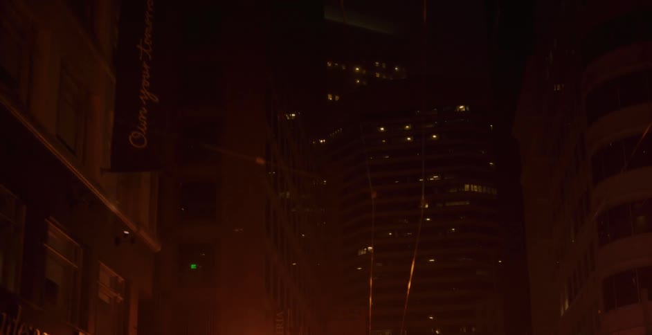 A slow, hazy, low-angle reveal of towering city skyscrapers illuminated by a warm glow on a dark night