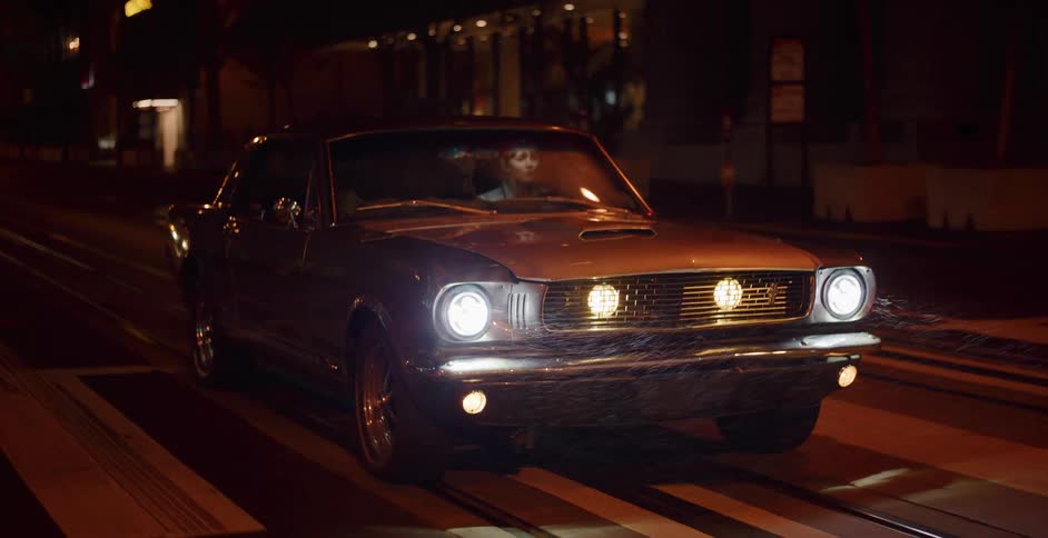 Cinematic shot of a young woman driving a classic muscle car down a city street at night