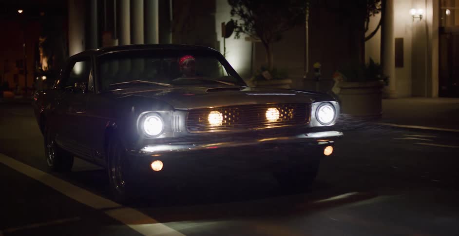 A young woman drives a classic Mustang through a misty downtown street late at night