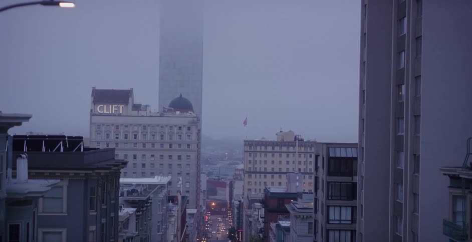 A high-angle view looking down a hilly street in San Francisco on a foggy evening as traffic flows below