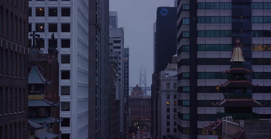 Atmospheric view of the San Francisco Bay Bridge seen through the fog between city buildings and Chinatown architecture at dusk