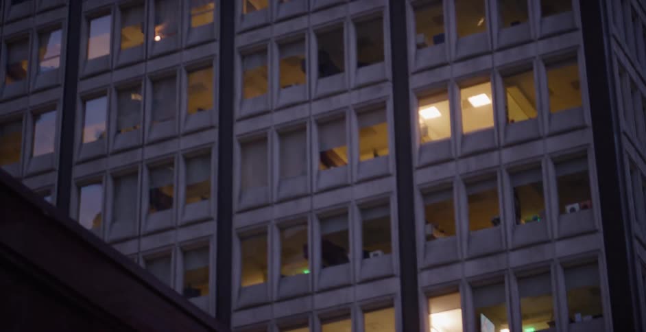 A slow pan across the illuminated windows of a city office building at dusk