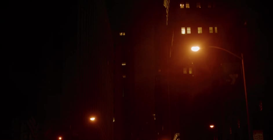 A slow tilt down a dark, foggy city street at night, illuminated by the orange glow of streetlights