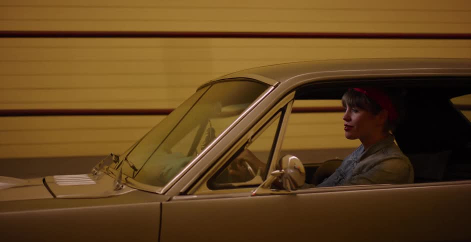 A smiling woman with a retro style drives a classic car through a city tunnel at night