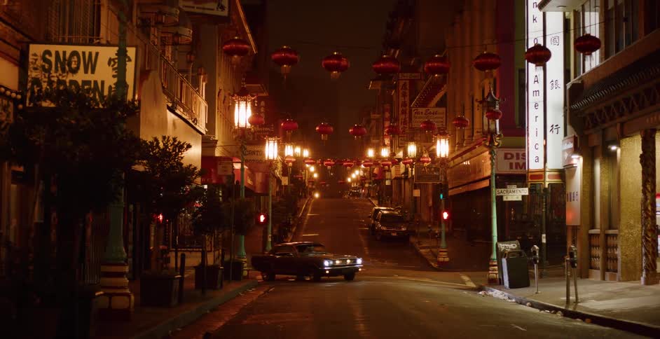 A vintage car with bright headlights stops on a deserted, lantern-adorned street in Chinatown at night