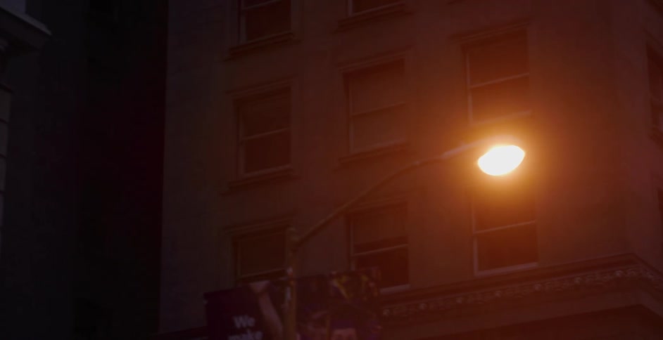The camera slowly pans across the dark facade of a city building at night, illuminated by a warm street lamp