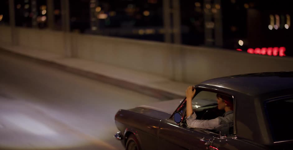 Side view of a woman driving a vintage sports car across a city bridge at night