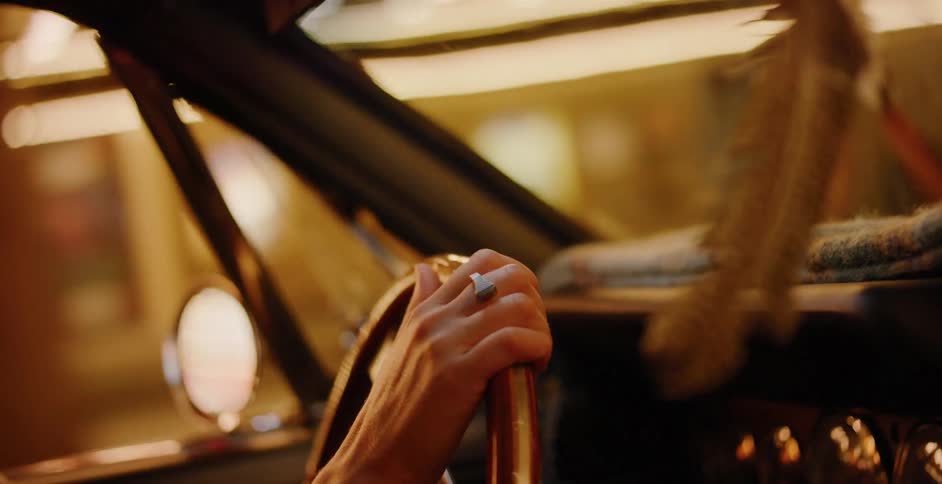 A cinematic close-up of a person's hand on a wooden steering wheel while driving a classic car through a lit tunnel at night